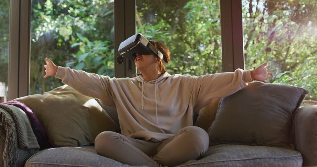 Asian girl smiling and gesturing while wearing vr headset sitting on the couch at home. entertainment and technology concept
