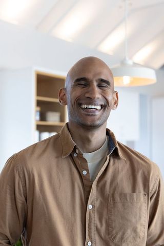 Smiling man with closed eyes in modern kitchen wearing brown shirt warm neutral interior