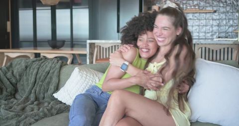 Multicultural friends hugging and laughing on sofa in bright modern living room