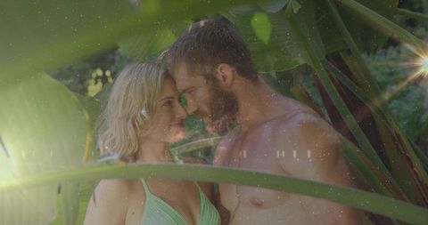 Couple sharing intimate moment among tropical palms with dreamy sun flare