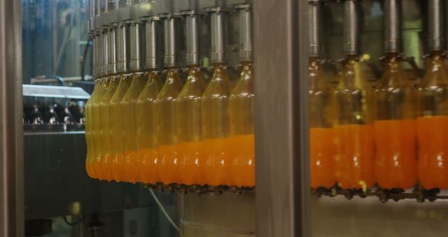 Industrial machine with plastic bottles being filled with orange juice. Food and drink industry concept.