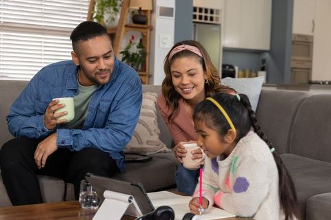 Diverse family bonding while child studying on tablet in modern living room
