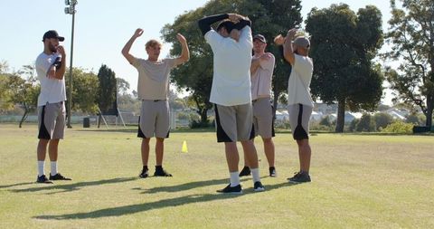 Male athletes warming up performing arm stretches on grass field with training cone