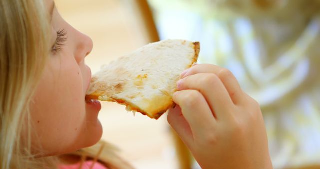 Child enjoying eating a slice of pizza. Ideal for use in advertising for food companies, family-oriented marketing, materials promoting kids’ snacks, or healthy eating guides. Highlights themes of childhood joy and meal times.