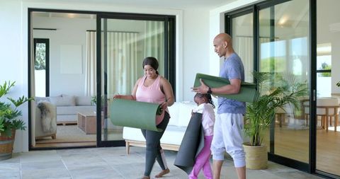 Diverse family practicing yoga on home patio, carrying rolled mats, wellness lifestyle