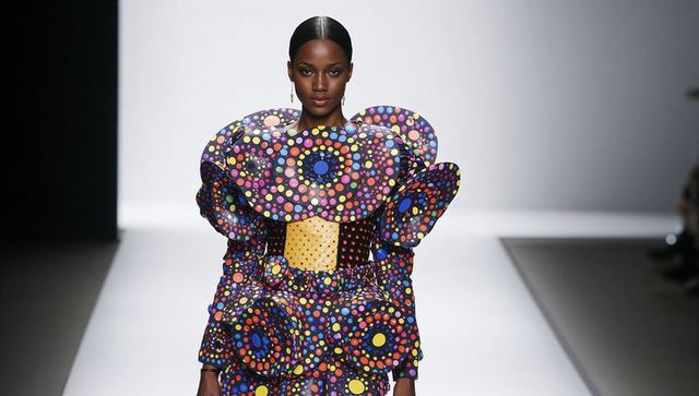 Modeling sculptural polka-dot couture dress with yellow waist panel on runway