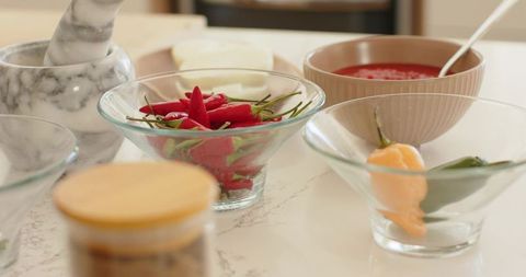 Fresh red chilies in glass bowl on marble countertop with sauce and mortar