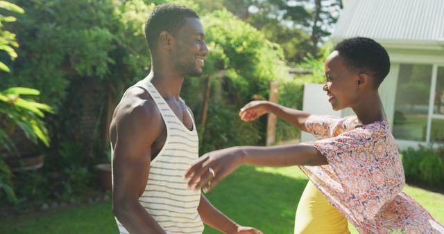 Picture of a happy couple dancing and smiling together in a sunlit garden filled with greenery. Perfect for use in content related to love, relationships, outdoor activities, summer, joy, and lifestyle themes.