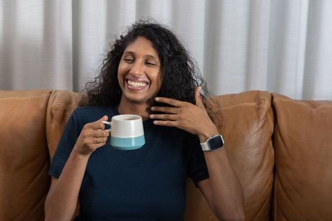 Smiling african american woman sipping coffee on leather sofa enjoying cozy morning vibe