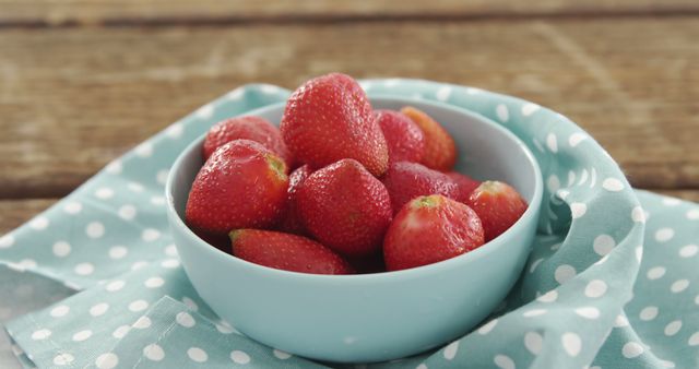 Delicious fresh strawberries sit in a light blue bowl, placed on a polka dot fabric. Ideal for advertisements related to healthy eating, kitchen décor, summer fruits, and organic farming. Perfect for use in articles about nutritious snacks, home gardening, and farm-to-table produce.
