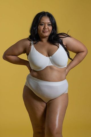 Curvy woman wearing white underwire bra and briefs posing confident on mustard backdrop