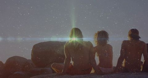 Friends Watching Sunset on Rocky Shore at Dusk with Lens Flare and Silhouette Mood
