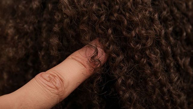 Pressing finger into dense dark brown curly hair showing strand texture and coil detail