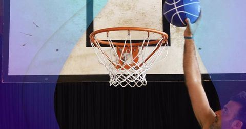 Adult man reaching to dunk blue basketball at indoor hoop with orange rim