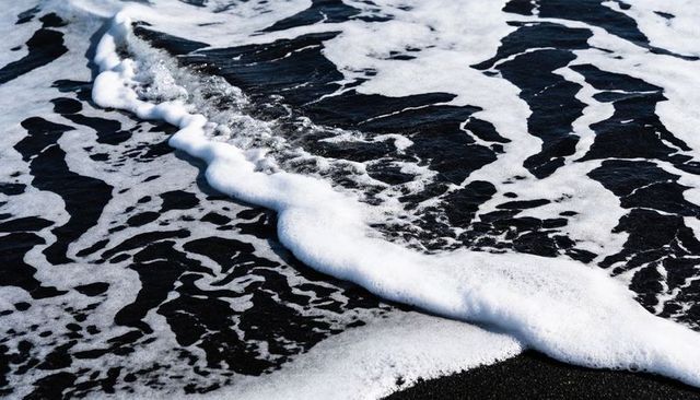 Foamy black sand shoreline with breaking wave and intricate ripple patterns