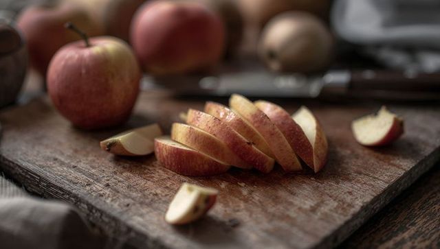 Fanned sliced red apple on rustic wooden cutting board, warm kitchen still life, knife