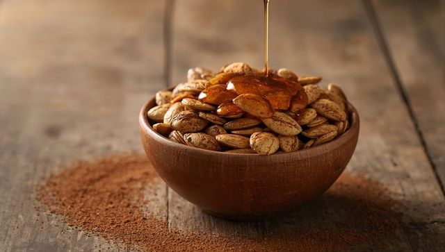 Drizzling Honey Over Toasted Pumpkin Seeds in Wooden Bowl