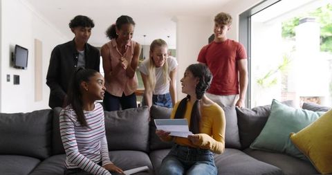 Sunlit modern living room friends exchanging card – diverse young adults celebrating