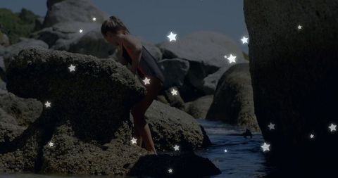 Child climbing barnacled boulders and wading into tidepool in one-piece swimsuit, exploration
