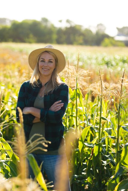 Portrait of caucasian mid adult female agronomist wearing hat with arms crossed standing in farm. summer, unaltered, agronomist, nature, organic farm and farming concept.