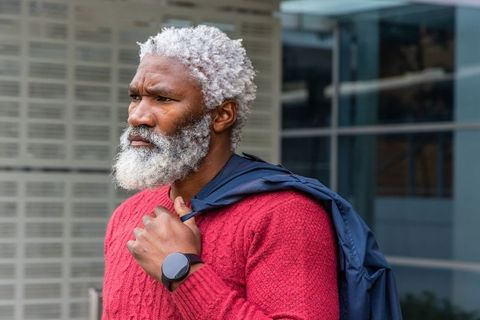 African american man standing in urban plaza wearing red knit sweater and smartwatch, contemplative