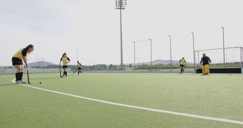 Female athletes competing in field hockey match under bright sky
