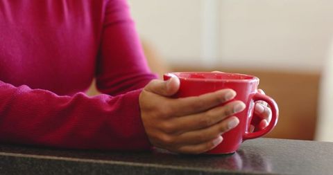 Cozy hands holding red ceramic mug on dark countertop with magenta sweater closeup