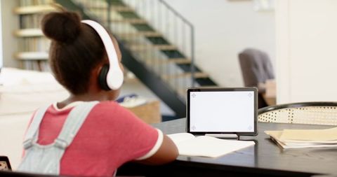 African american child studying at home with tablet and headphones at dining table
