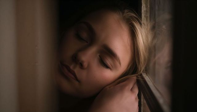 Adult woman resting cheek on windowpane holding hair in soft natural light portrait