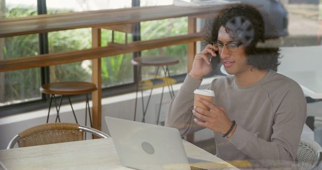 Man With Curly Hair Working on Laptop While Talking on Phone and Drinking Coffee - Download Free Stock Images Pikwizard.com