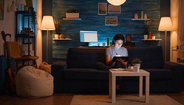 Teen using tablet and stylus on dark sofa at night home office cozy study session