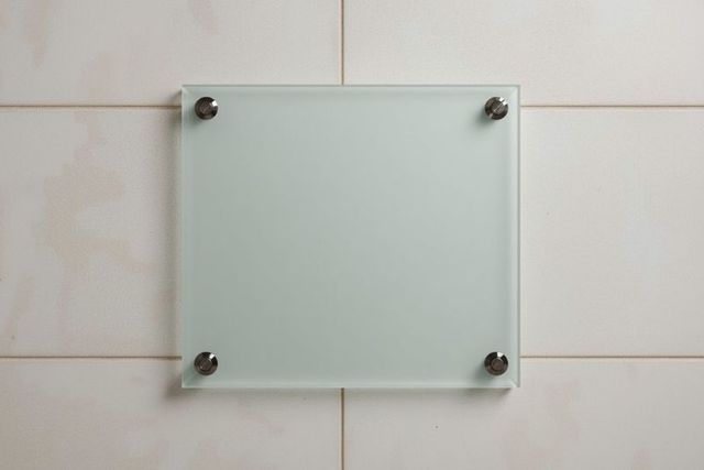 Frosted glass panel on beige tiled wall with metal standoffs