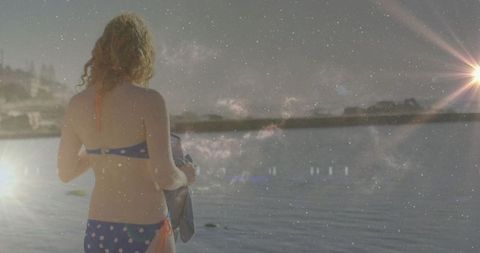 Woman in polka-dot bikini admiring scenic lakeside with sun glare