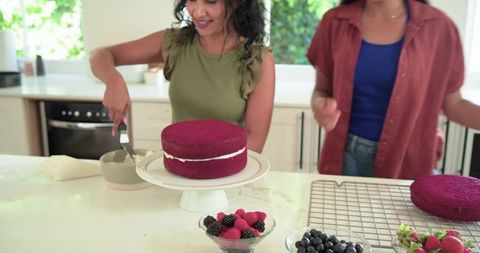 Spreading frosting and assembling red velvet layer cake in sunlit home kitchen