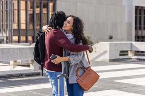 Couple embracing on city plaza with luggage and smartphones, joyful reunion outdoors