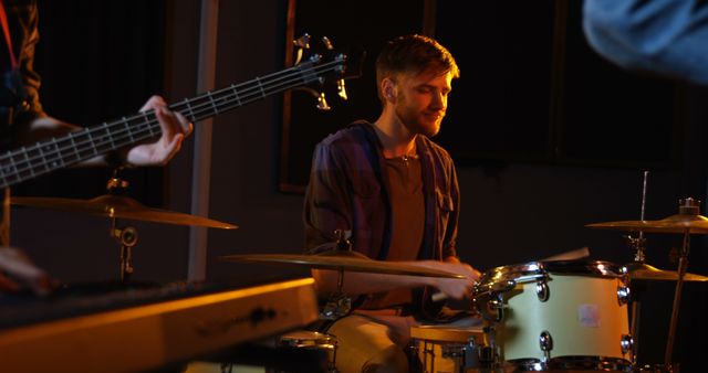 Young drummer practicing with his bandmates in a dimly lit studio. Ideal for content related to music production, band rehearsals, musical talent, and professional musician profiles.