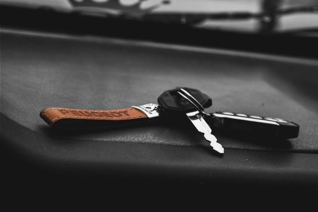 Car keys with a decorative leather keychain lying on a car's dashboard. The focus on the keys and keychain highlights automobile security and driving equipment. Ideal for use in automotive advertisements, security system promotions, and transportation-themed articles.