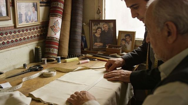 Tailors measuring and marking fabric on wooden bench in traditional workshop