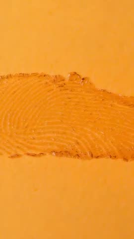 Vertical macro motion revealing glossy viscous print smear and ridge texture on orange surface