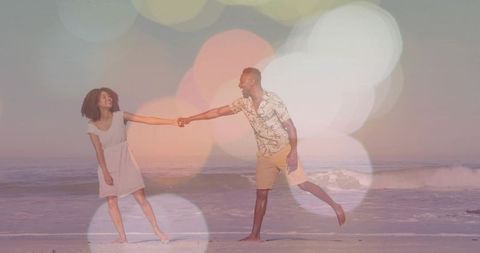 Couple holding hands on sunset beach with bokeh light overlay, romantic barefoot stroll
