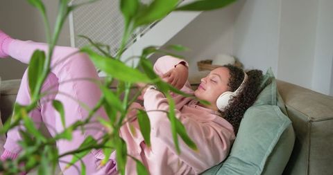 African american woman relaxing on sofa with headphones and houseplant in cozy living room