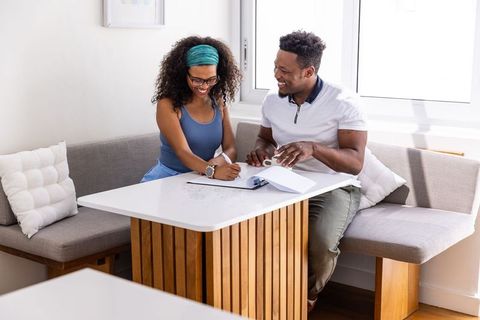 Diverse couple reviewing documents and signing forms at bright home dining nook