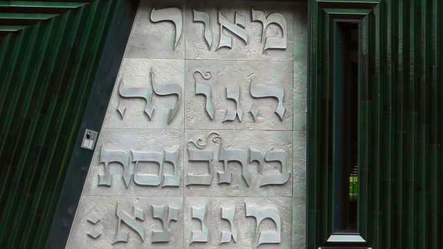 Close-up view of Hebrew script carved into walls of modern architectural exterior. Suitable for use in educational content, articles on cultural heritage, Jewish community newsletters, language studies, or features on unique urban designs.