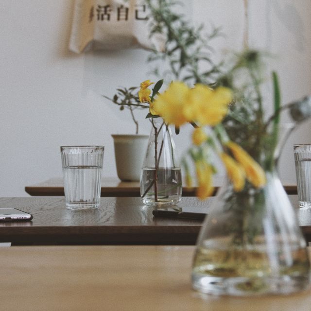 Features minimalist cafe table setting with clear glasses of water and yellow flowers. Perfect for promoting cafes, lifestyle blogs, interior design inspiration, and wellness-themed projects. Ideal for illustrating cozy and serene environments in urban settings.