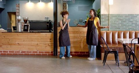 Two baristas chatting behind wooden counter in modern coffee shop with espresso machine
