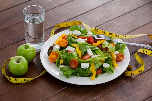 Salad, apple and measuring tape on table - diet concept
