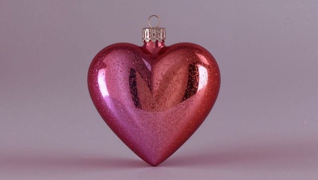 Glossy pink heart ornament with glitter and silver cap on pastel tabletop