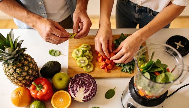Couple preparing fresh fruit and veggies for smoothie on kitchen countertop with blender