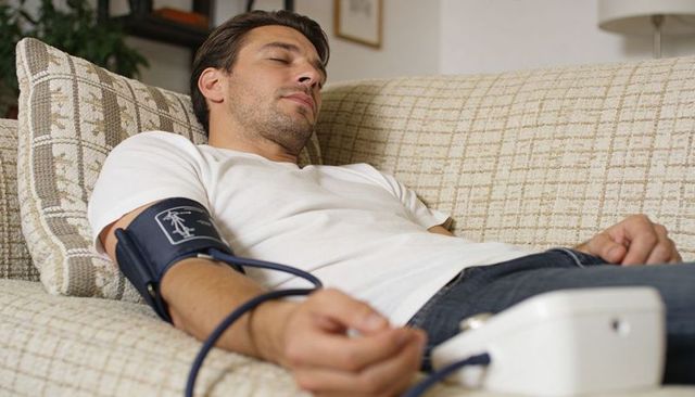 Young man resting on sofa measuring blood pressure with home monitor for wellness