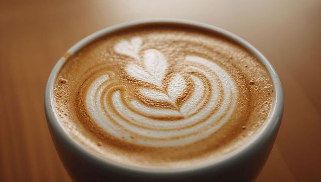 Close-up ceramic cup featuring latte art rosette and heart on warm wooden table